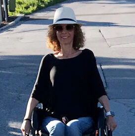 Katja Naumann, eine junge Dame im Rollstuhl, hier mit weißem Hut, lachend, in der Sonne